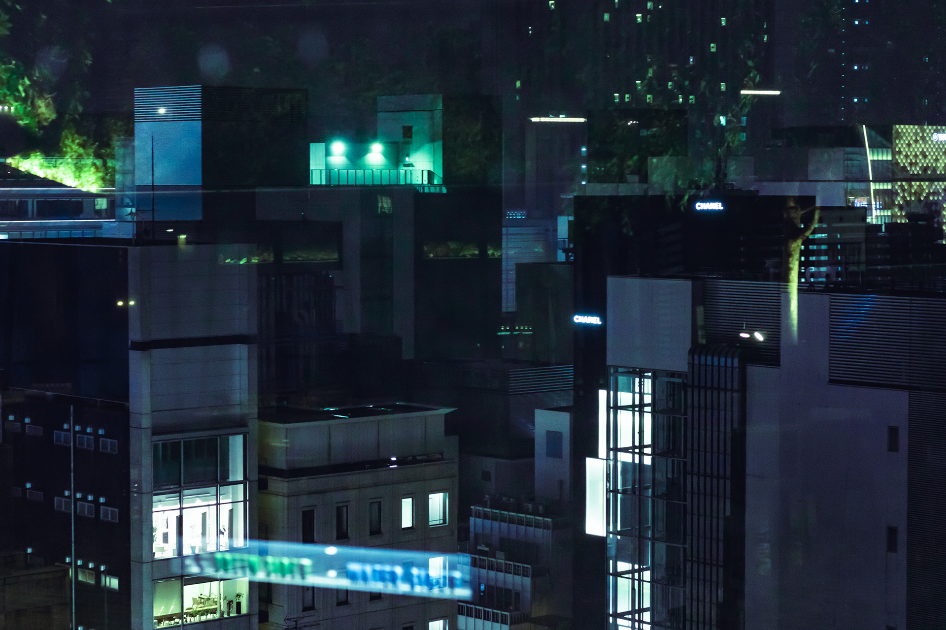 Night time view from a rooftop of modern buildings with bright green reflections in glass in the foreground.